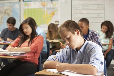 Male Pupil Studying At Desk In Classroom